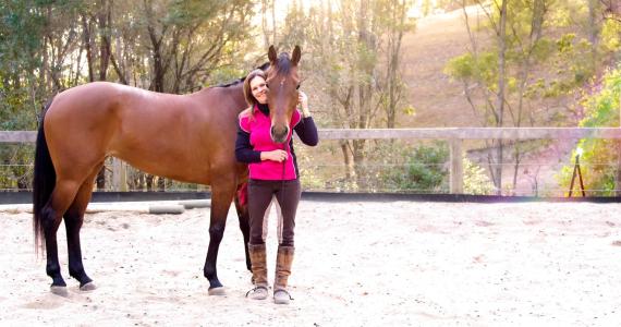 a woman holding a brown horse standing next to a fence